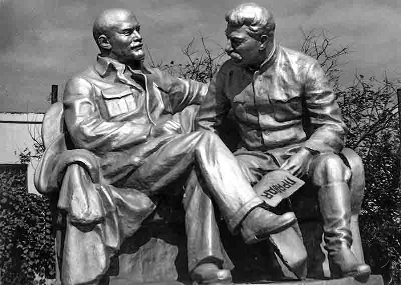 A black and white image depicting two men (Lenin and Stalin) seated on a statue, capturing a moment of leisure and camaraderie.