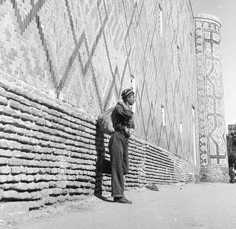 A monochrome photograph showcasing Uzbek man standing beside a textured brick wall, showcasing a casual pose against the sturdy backdrop.