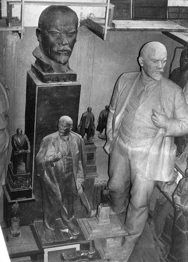 A monochrome photograph capturing a room filled with Lenin statues, highlighting their forms and the ambiance of the space.