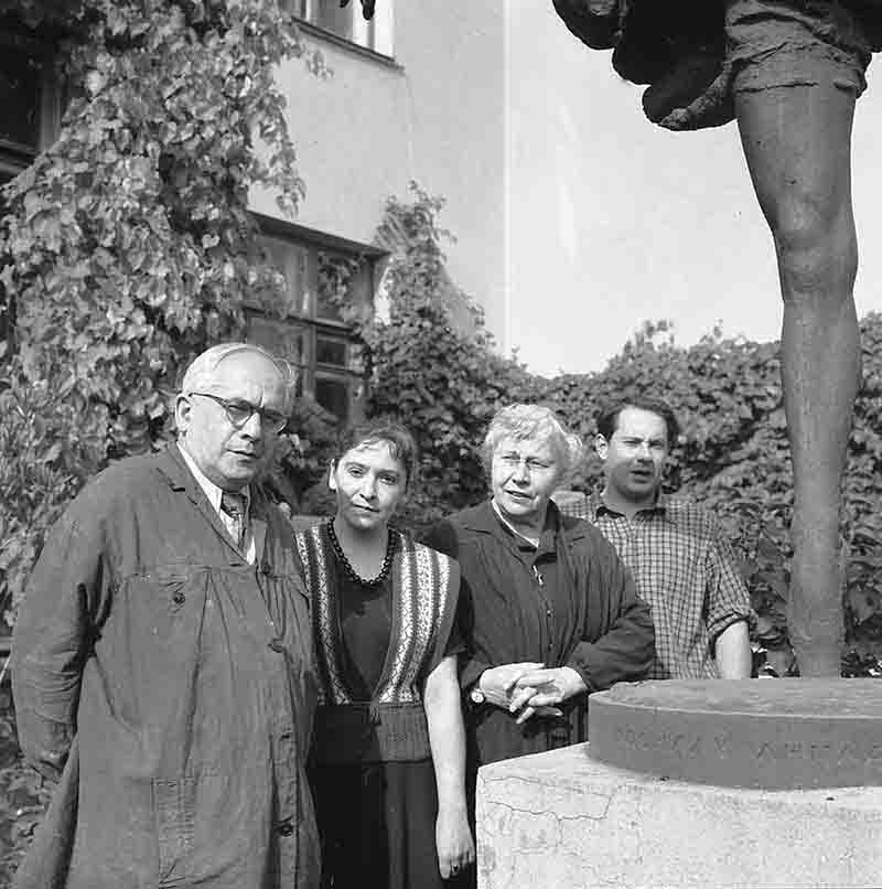 A black and white image featuring four individuals standing beside a soviet statue, capturing a moment of contemplation and presence.