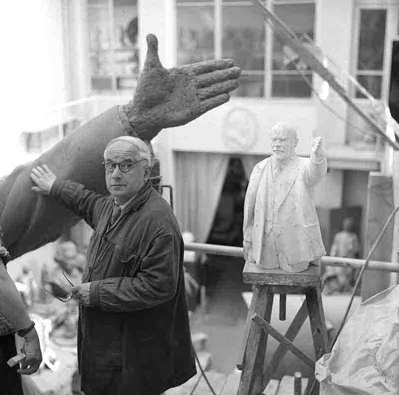 Sculptor Manizer stands beside a large statue of a hand, showcasing the intricate details and craftsmanship of the sculpture.