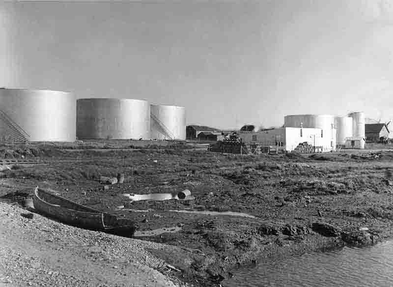 A monochrome photograph depicting Baku Azerbaijan oil tanks and a boat, illustrating the intersection of industry and water transport.