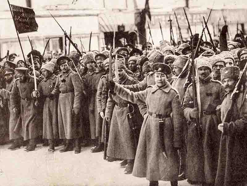 The Russian Revolution of 1917: The photograph captures a large group of revolutionary soldiers standing in a line, many of them holding rifles with bayonets fixed. Soldiers of the Bolshevik uprising are dressed in long coats and fur-lined hats, and several are holding swords or sabers.
