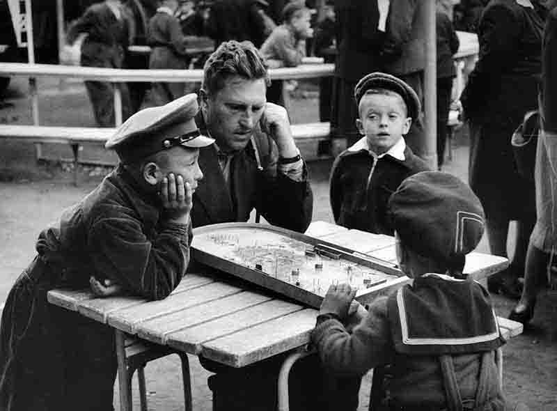 A soviet man and two boys seated at a table, playing a boardgame, showcasing a moment of fun and interaction among them.