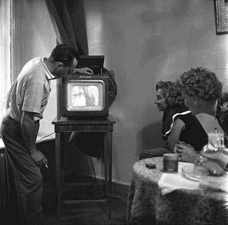 A monochrome photograph showcasing a man and two women in a cozy soviet union living room, watching television.