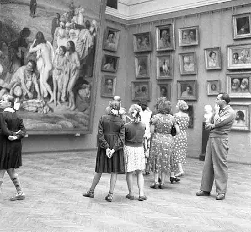 A monochrome photograph showcasing a gathering of people admiring and contemplating artworks at the State Hermitage Museum, St. Peterburg art gallery.