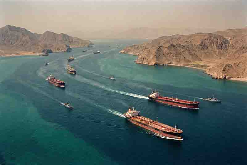 Aerial view of the Strait of Hormuz between Iran and Oman, showing oil tankers transiting the narrow passage — the world's most strategic energy chokepoint during the Cold War.