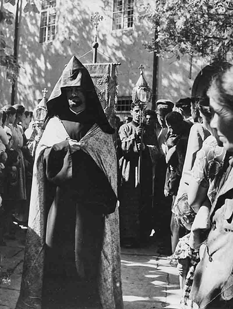 A black and white photo of a religious procession of Armenian Apostolic Christianity. The focal point is Vazgen I in a long, dark, hooded robe (known as a kuku or varkas) and an embroidered or patterned cape.